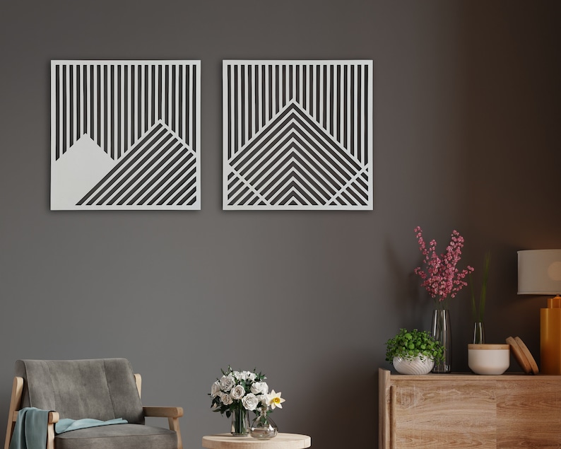 May include: Two white geometric wall art pieces with a black and white striped pattern. The pieces are hanging on a grey wall above a wooden dresser.