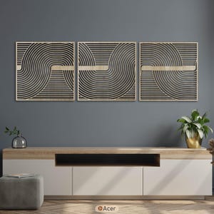 May include: Three square wooden wall art pieces with a geometric design of curved black lines and a light wood accent. The artwork is displayed above a white and wood-toned cabinet, with plants and decor.