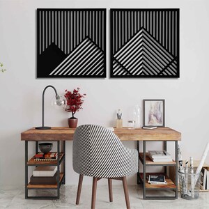 May include: Two black and white geometric wall art pieces with a striped pattern. The art is hanging on a white wall above a wooden desk with a black metal frame. The desk has a chair with a black and white striped pattern.