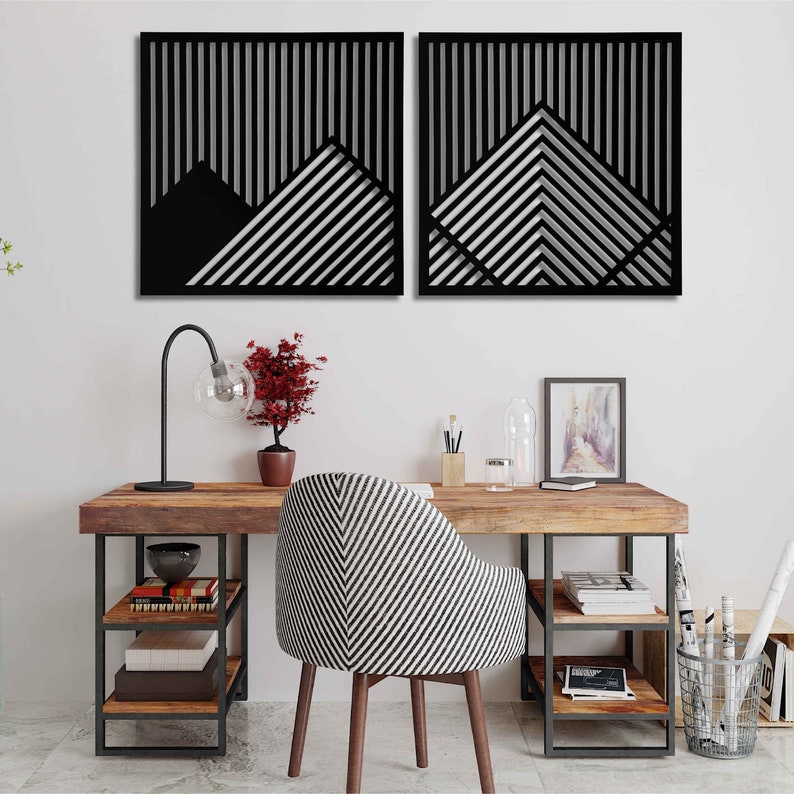 May include: Two black and white geometric wall art pieces with a striped pattern. The art is hanging on a white wall above a wooden desk with a black metal frame. The desk has a chair with a black and white striped pattern.