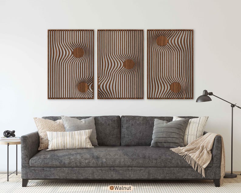 May include: Three framed wooden wall art pieces with a wavy, striped design and circular cutouts. The frames are a dark brown, and the artwork is mounted above a gray sofa with decorative pillows.