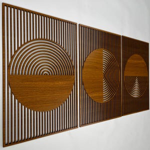 Op de afbeelding: Drie houten wandkunstpanelen met een geometrisch ontwerp. Elk paneel heeft een donkerbruin houten frame met verticale lamellen. De panelen hebben cirkelvormige en halfronde uitsparingen in lichter bruin hout.