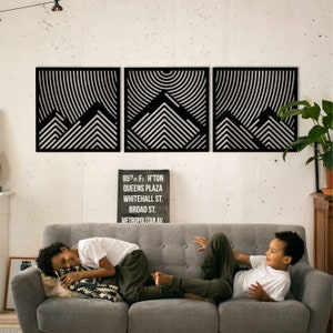 May include: Three black and white geometric wall art pieces with a mountain design. The art is hung on a white wall above a gray couch with two children sitting on it.