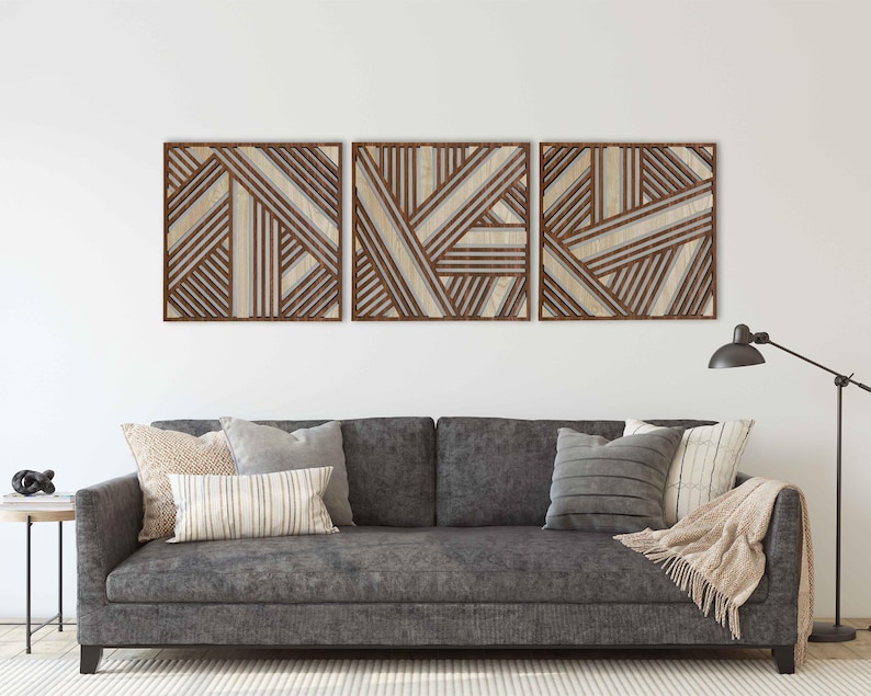 May include: Three brown wood wall decor panels with a geometric pattern of intersecting lines. The panels are arranged horizontally and are hanging on a white wall above a gray couch with pillows.