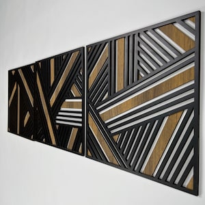 May include: A three-piece geometric wall art set with black and brown wood panels. The panels feature a modern abstract design with intersecting lines and shapes.