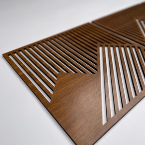 May include: Two brown wooden wall panels with a geometric pattern of diagonal lines cut out. The panels are made of wood with a dark brown stain.