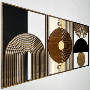 May include: Set of three geometric wall art panels. Each panel features a wooden frame with a unique design. One panel has a black and white background with a layered arch. The other panels have circular and semi-circular designs.