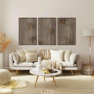 May include: Three wooden wall art panels with a wavy, textured design and a circular accent. The panels are displayed above a light-colored sofa with decorative pillows and a throw blanket. The room has a neutral color palette.