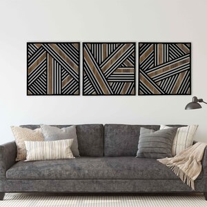 May include: Three black framed wall art pieces with a geometric pattern of brown and white stripes. The art is hung above a gray couch with pillows and a throw blanket.