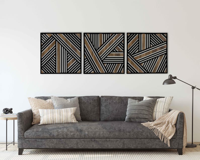 May include: Three black framed wall art pieces with a geometric pattern of brown and white stripes. The art is hung above a gray couch with pillows and a throw blanket.
