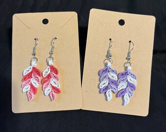 Può includere: Due paia di orecchini pendenti con un design a foglia. Un paio è rosa, bianco e rosso, l'altro paio è viola, bianco e crema.