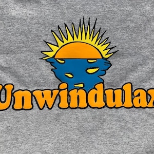 Puede incluir: Una camiseta gris con un sol naranja y amarillo poniéndose sobre un cuerpo de agua azul. El texto "Unwindulax" está impreso en naranja con un contorno negro.