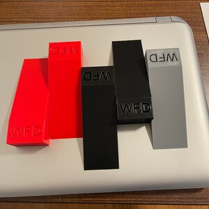 May include: Four small blocks with the letters "WFD" printed on them. The blocks are red, black, grey, and black. The blocks are arranged in a row on a silver surface.