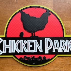 May include: A yellow, red, and black sign with the text "Chicken Park" in white letters. A black silhouette of a chicken with an egg is in the center of the sign.