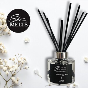 May include: A clear glass reed diffuser with black reeds and a silver collar. The label reads "She Melts" and "Lemongrass & Lime". White flowers and petals are scattered around the diffuser on a white background.