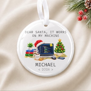 May include: A round white ceramic ornament with a white ribbon hanger. The design features a laptop with code, a stack of books, a mug, a cookie, and a Christmas tree. Text reads: DEAR SANTA, IT WORKS ON MY MACHINE, MICHAEL, and 2026.