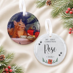 May include: Two round ceramic ornaments with white ribbon hangers. One ornament features a photograph of an orange tabby cat sitting near red and gold wrapped gifts. The other white ornament displays the text My First Christmas Rose 2026.