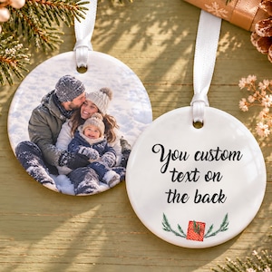 May include: Two round white ceramic ornaments with white ribbon hangers. One ornament features a color photograph of a family in a snowy landscape. The other ornament displays the black text You custom text on the back above a small red gift icon.