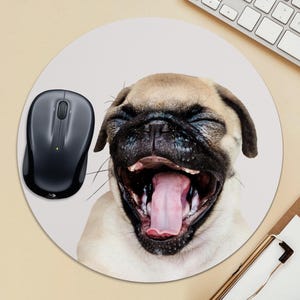 May include: A round mouse pad with a white background featuring a close-up image of a pug dog with its mouth open and tongue sticking out. A black wireless computer mouse is on the left side of the mouse pad.