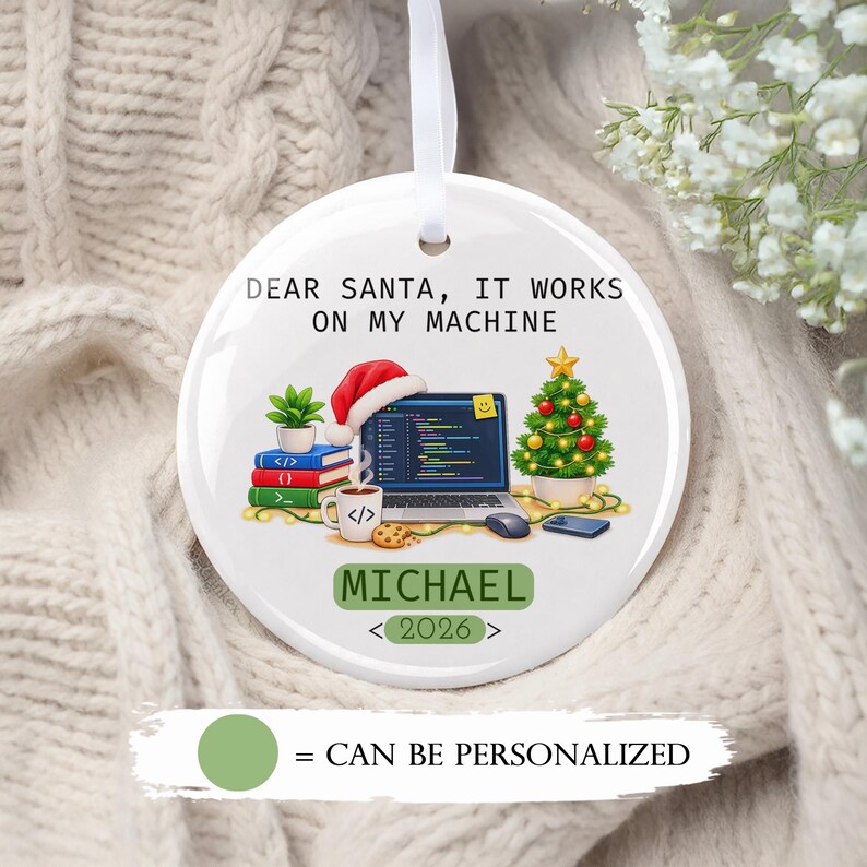 May include: A round white ceramic Christmas ornament featuring the text DEAR SANTA, IT WORKS ON MY MACHINE. The graphic shows a laptop with code, a Santa hat, a stack of books, a coffee mug, a Christmas tree, and the name MICHAEL with 2026.