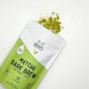 May include: A white pouch with a green label that says "Matcha Bark Brew for Dogs + Cats". The pouch is open and green powder is spilling out.