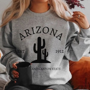 May include: Gray sweatshirt with black text that reads "Arizona Est 1912 and Canyon State" with a black silhouette of two cacti.
