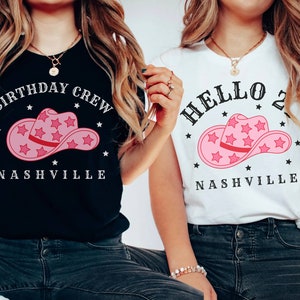 May include: Two women wearing t-shirts with a pink cowboy hat graphic and the text "Birthday Crew Nashville" and "Hello 2 Nashville".