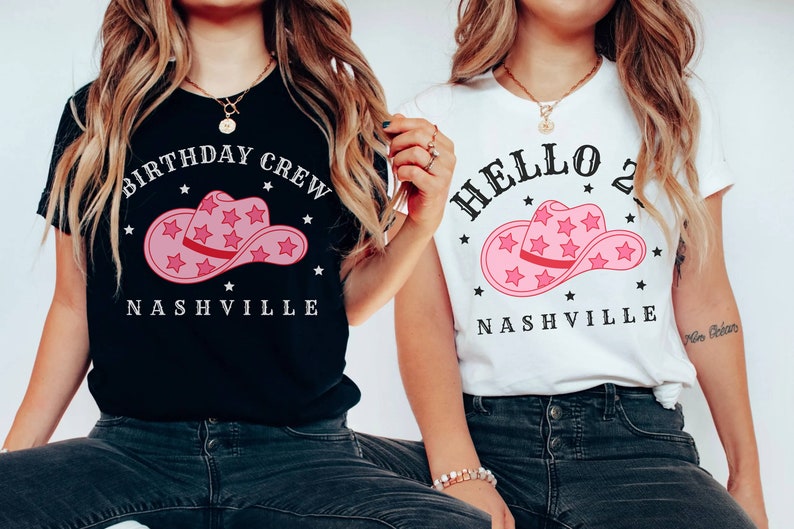 May include: Two women wearing t-shirts with a pink cowboy hat graphic and the text "Birthday Crew Nashville" and "Hello 2 Nashville".