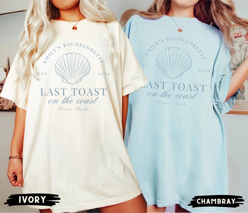 K&ouml;nnte beinhalten: Zwei &uuml;bergro&szlig;e T-Shirts mit einem Muschel-Motiv und dem Text "Emily's Bachelorette Est 2024 Last Toast on the Coast Miami Florida". Die T-Shirts sind in Elfenbein und Hellblau.