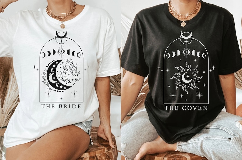 Op de afbeelding: Twee witte T-shirts met zwarte grafische ontwerpen. Het linker shirt heeft een halve maan en sterren met de tekst "THE BRIDE". Het rechter shirt heeft een zon en een maan met de tekst "THE COVEN".