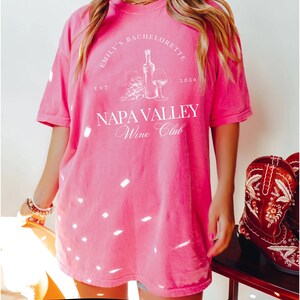 May include: Pink oversized t-shirt with white text that reads "Emily's Bachelorette Est. 2024 Napa Valley Wine Club". The shirt features a graphic of a wine bottle and glass.