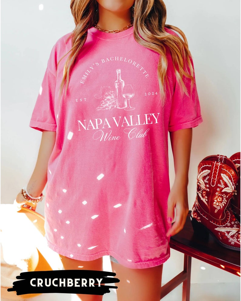 May include: Pink oversized t-shirt with white text that reads "Emily's Bachelorette Est. 2024 Napa Valley Wine Club". The shirt features a graphic of a wine bottle and glass.