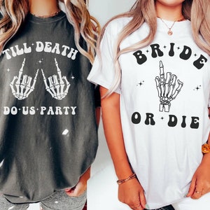 May include: Two t-shirts with a skeleton hand graphic and text. The first shirt is dark gray with the text "Till Death Do Us Party". The second shirt is white with the text "Bride or Die".