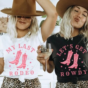 Puede incluir: Dos mujeres con camisetas con gr&aacute;ficos de botas de vaquero. Una camiseta es blanca con el texto "My Last Rodeo", la otra es negra con "Let's Get Rowdy". Ambas camisetas tienen texto y dise&ntilde;os de botas rosas.