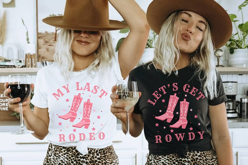 Puede incluir: Dos mujeres con camisetas con gr&aacute;ficos de botas de vaquero. Una camiseta es blanca con el texto "My Last Rodeo", la otra es negra con "Let's Get Rowdy". Ambas camisetas tienen texto y dise&ntilde;os de botas rosas.