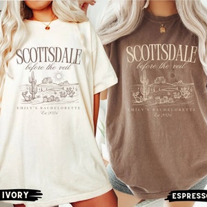 May include: Two oversized t-shirts with a desert landscape graphic and the text "Scottsdale before the veil" and "Emily's Bachelorette Est 2024". The shirts are shown in ivory and espresso colors.