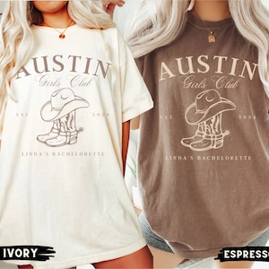 May include: Two t-shirts with the text "Austin Girls Club" and a graphic of a cowboy boot and hat. The text "EST 2024" and "Linda's Bachelorette" are also included. The t-shirts are in ivory and espresso colors.
