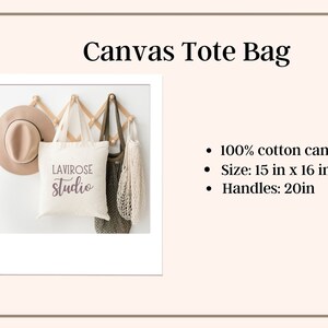 May include: A white canvas tote bag with the text "LAVIROSE studio" printed in purple. The bag is hanging on a wooden rack with a brown hat and a green mesh bag. The bag is 15 inches by 16 inches with 20-inch handles.