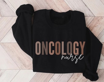 Könnte beinhalten: Schwarzer Pullover mit dem Text "ONCOLOGY nurse" in braunen und weißen Buchstaben.