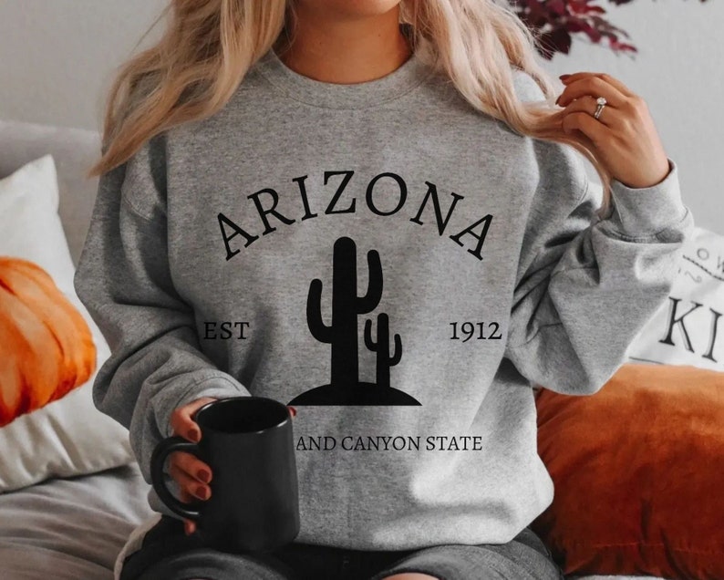 May include: Gray sweatshirt with black text that reads "Arizona Est 1912 and Canyon State" with a black silhouette of two cacti.
