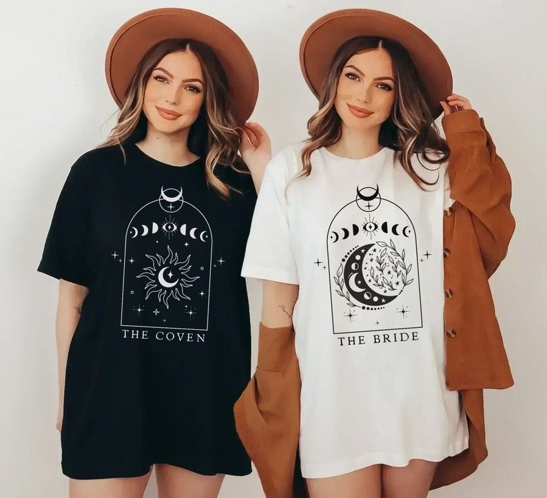 Op de afbeelding: Twee vrouwen dragen zwarte en witte T-shirts met maan- en stermotieven. Het zwarte T-shirt zegt "The Coven" en het witte T-shirt zegt "The Bride".