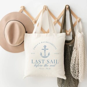 May include: A white tote bag with blue text and an anchor graphic. The text reads "Emily's Bachelorette Est 2024 Last Sail Before the Veil Miami, Florida".