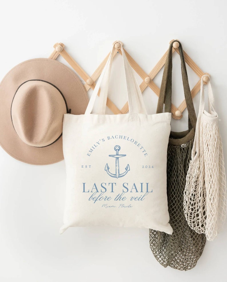 May include: A white tote bag with blue text and an anchor graphic. The text reads "Emily's Bachelorette Est 2024 Last Sail Before the Veil Miami, Florida".