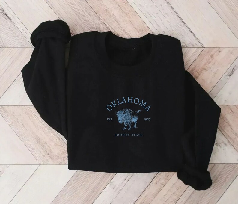 Puede incluir: Sudadera negra con un estampado gr&aacute;fico azul y blanco de un b&uacute;falo con el texto "Oklahoma Est 1907 Sooner State"
