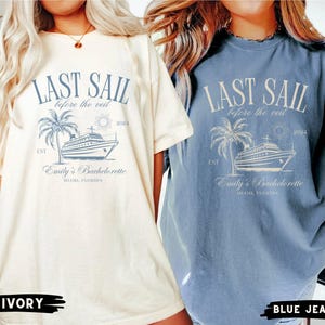 May include: Two white and blue t-shirts with a graphic of a cruise ship and the text "Last Sail Before the Veil" and "Emily's Bachelorette". The t-shirts are shown on models wearing them. The white t-shirt is labeled "Ivory" and the blue t-shirt is labeled "Blue Jean".