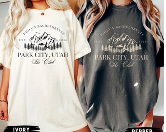 May include: Two oversized t-shirts with a mountain graphic and the text "Emily's Bachelorette Est 2024 Park City, Utah Ski Club". The t-shirts are in ivory and pepper colors.