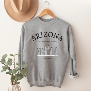 May include: Gray sweatshirt with a black graphic design that says "Arizona, The Grand Canyon State, Est 1912" with a drawing of cacti.