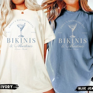 Puede incluir: Dos camisetas de gran tama&ntilde;o con un dise&ntilde;o gr&aacute;fico azul. El texto en las camisetas dice "Emily's Bachelorette Est 2024 Bikinis & Martinis Miami Florida". Las camisetas se muestran en colores marfil y azul vaquero.