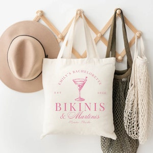 Puede incluir: Bolsa de lona blanca con texto rosa que dice "Emily's Bachelorette Est. 2024 Bikinis & Martinis Miami, Florida". La bolsa presenta una ilustraci&oacute;n rosa de una copa de martini con aceitunas.