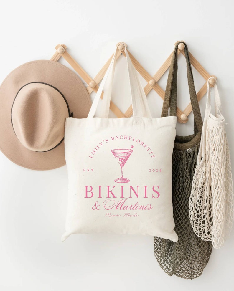 Puede incluir: Bolsa de lona blanca con texto rosa que dice "Emily's Bachelorette Est. 2024 Bikinis & Martinis Miami, Florida". La bolsa presenta una ilustraci&oacute;n rosa de una copa de martini con aceitunas.